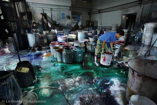 A man is working in a dye factory in China with buckets of chemical dyes for use in the fast fashion industry.