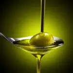 Olive oil being poured into a spoon that is holding an olive.