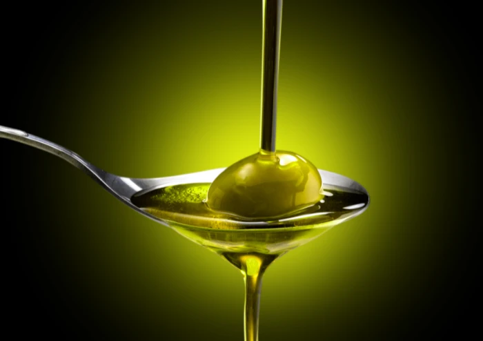 Olive oil being poured into a spoon that is holding an olive.