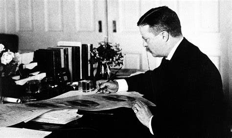 President Theodore Roosevelt in a suit sitting at a desk with papers.