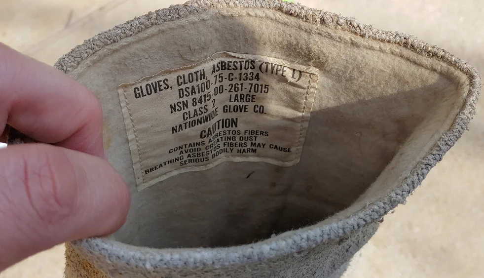 Close-up of a label inside an asbestos cloth glove, warning about asbestos fibers. Asbestos gloves were once common for heat protection in industries like metalworking and firefighting, but they exposed users to serious health risks.